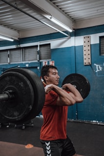 A focused CrossFit athlete performing a clean and jerk in a gym with red, white, and black accents.