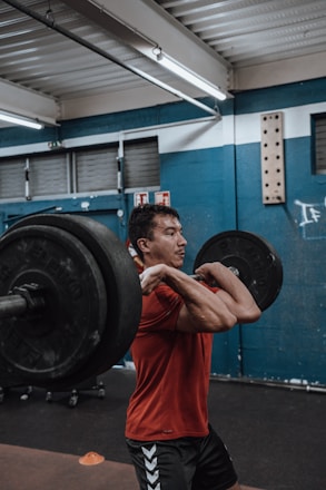 Athlete performing a clean and jerk in a gym with red, black, and white branding.