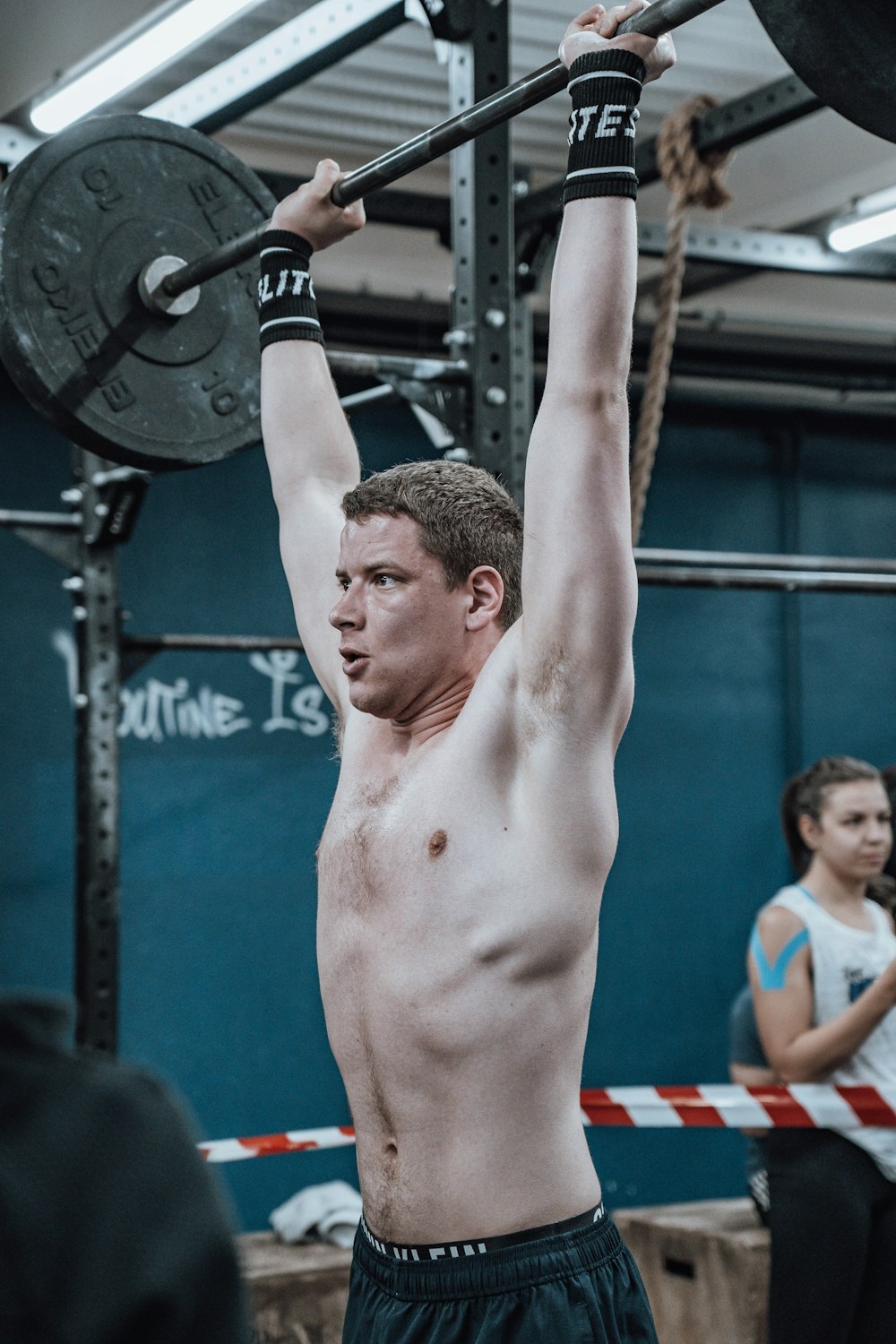 Un hombre sin camisa levantando una barra en un gimnasio