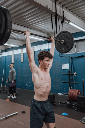 Close-up of a trainer correcting a gym member's posture during a weightlifting exercise.