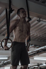 Close-up of a male athlete gripping heavy gymnastic rings in a dimly lit training facility.
