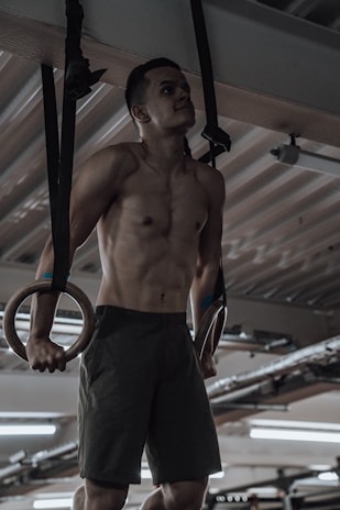 A focused athlete performing a perfect muscle-up on gymnastic rings against a clear blue sky.