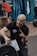 A person with a bald head and a beard is crouching and smiling, pointing a finger upwards. They are wearing a black t-shirt with 'French Throwdown 2024' written on it. A weight plate is visible in the foreground, and other people are exercising in the background in a gym setting.
