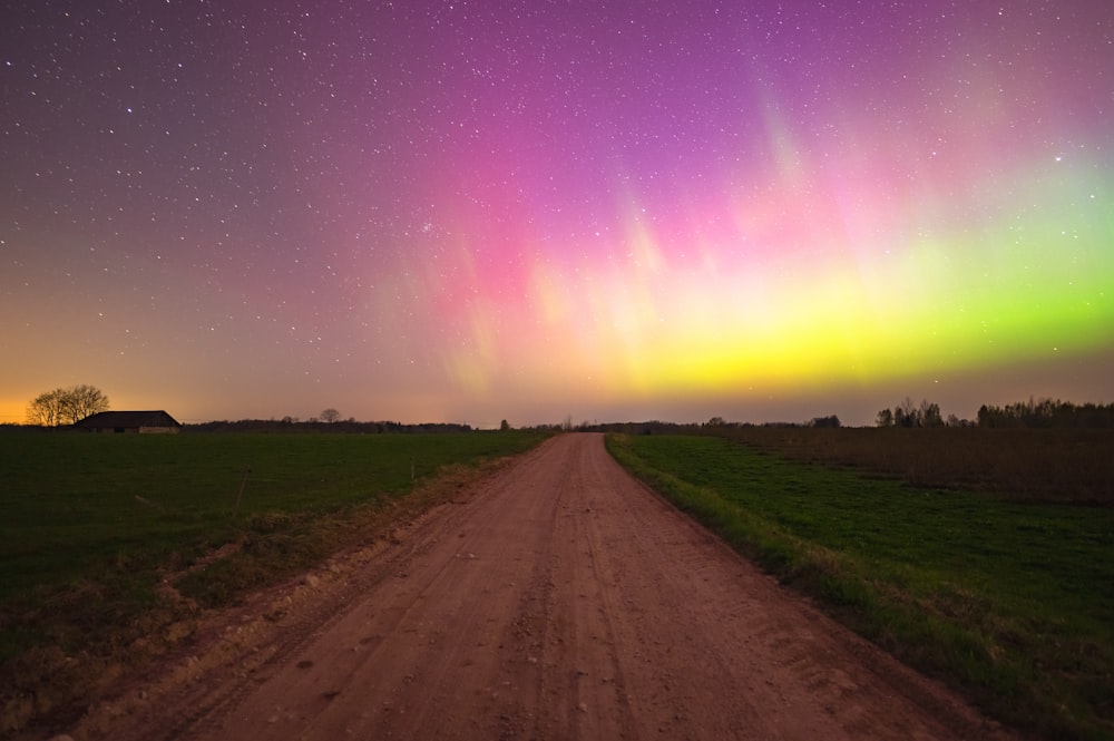 a dirt road with a green and purple aurora light in the sky