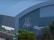 A large building with a corrugated metal exterior features a prominent logo displaying the letter 'A' in bold colors. Below the logo, the words 'Cole and Jeannie Davis Sports Center' are illuminated. Trees and a street sign are visible in the foreground.
