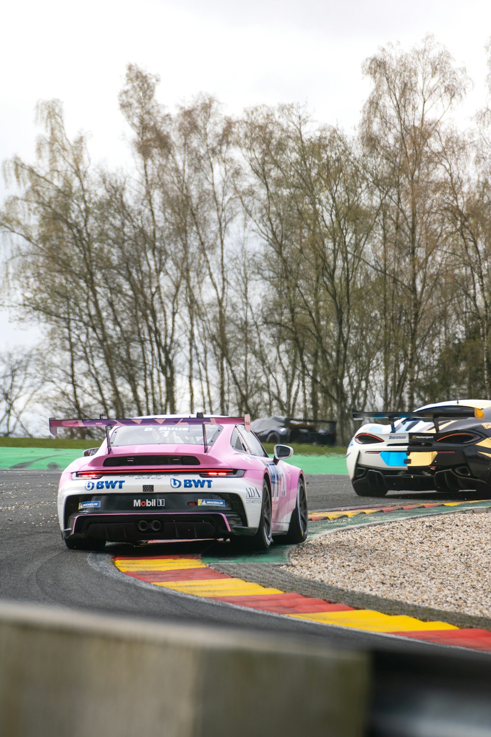 two racing cars on a race track with trees in the background