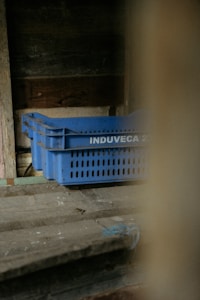 A set of blue plastic crates with the label 'INDUVECA 2' is placed in a dimly lit, rustic environment. The wooden walls and surfaces have a weathered appearance, adding to the rustic feel.