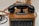 An antique rotary-style telephone rests on a wooden base with visible cords and a series of labeled switches, possibly indicating a multi-line or switchboard functionality.