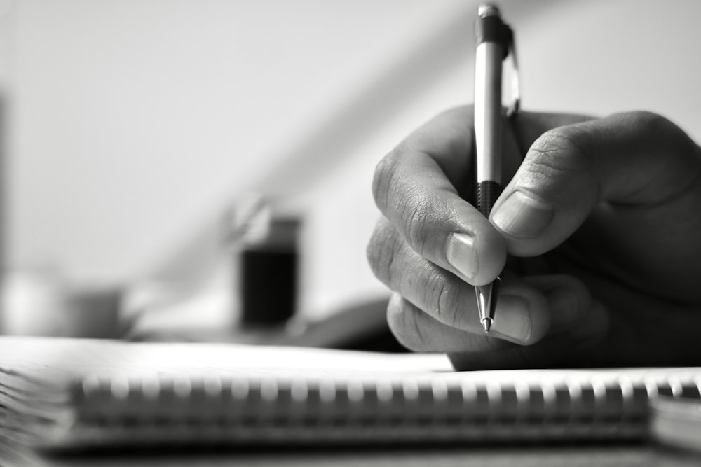 a person writing on a notebook with a pen