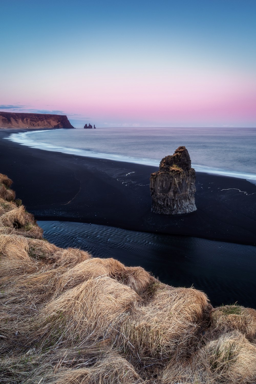 a black sand beach with a cliff in the distance