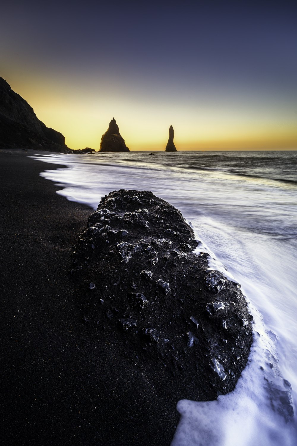 a black sand beach with a rock formation in the foreground