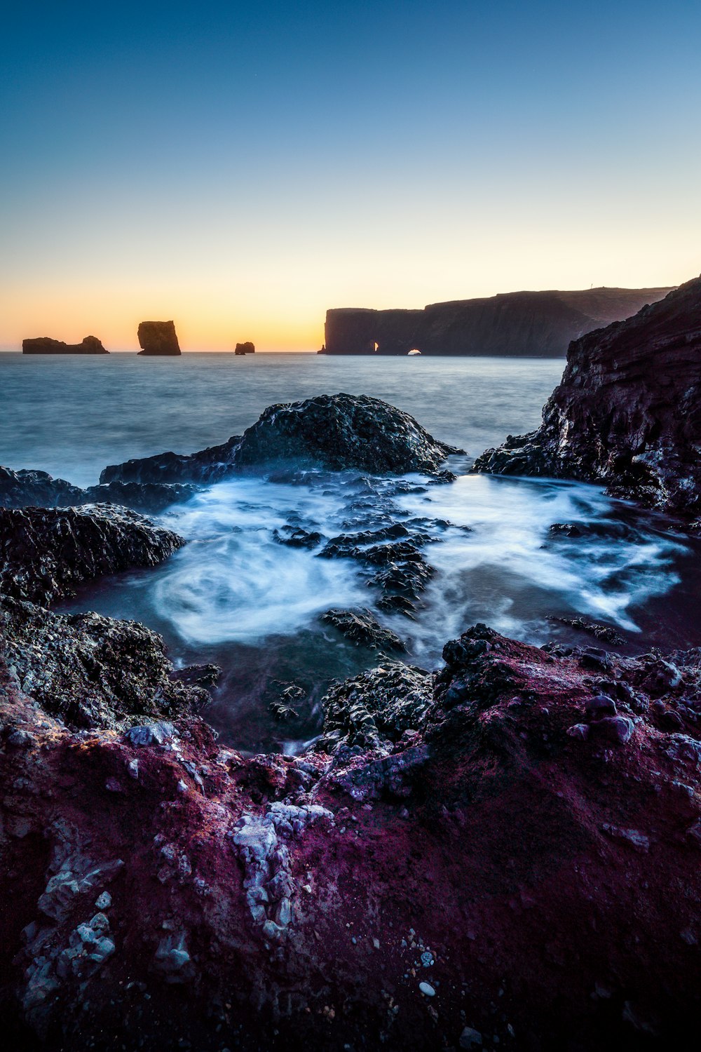 the sun is setting over the ocean and rocks