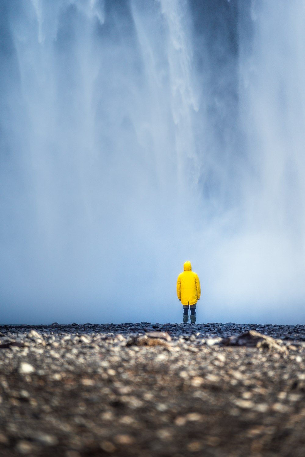 Ein Mann in einer gelben Jacke steht vor einem Wasserfall