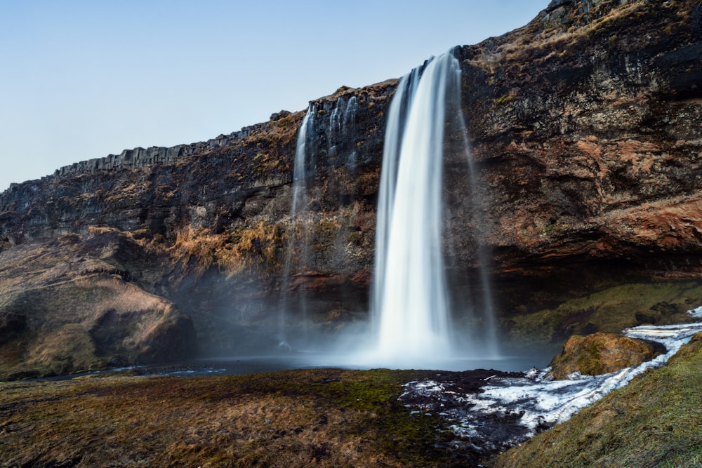 a large waterfall with snow on the ground