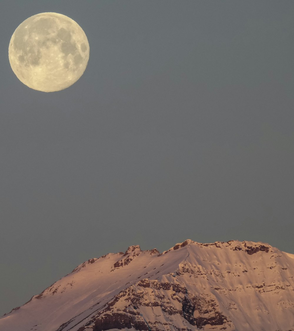 a full moon rising over a snowy mountain