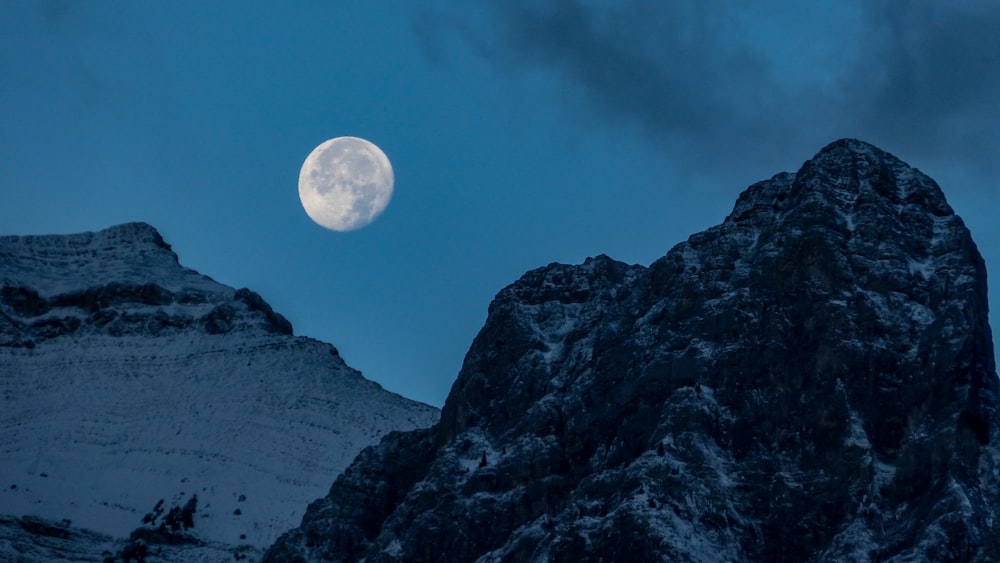a full moon is seen above a snowy mountain
