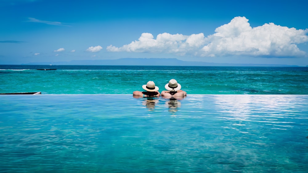 two people sitting on the edge of a swimming pool