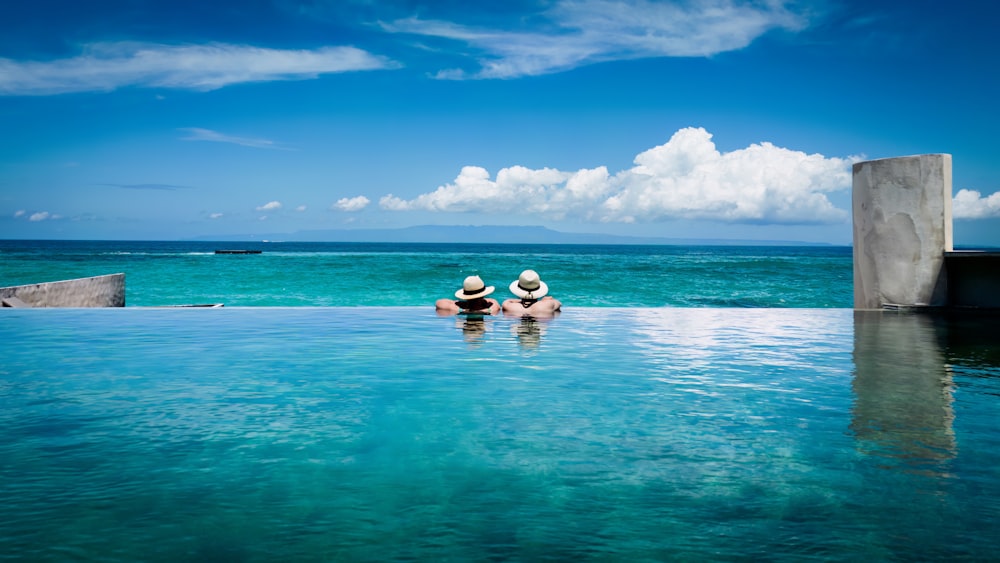 two people sitting on the edge of a swimming pool