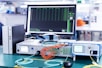 A laboratory setup featuring various networking and testing equipment on a table. A computer monitor displaying test results with a 'Pass' message is prominently positioned. Multiple cables in orange and blue are connected to devices labeled 'Optical Phase Modulation Meter' and 'Test Station'. The environment appears clean and organized, suggesting a professional or industrial setting.