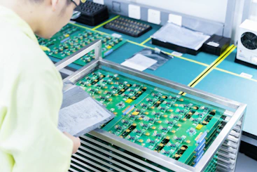 Technician inspecting a MacBook motherboard under bright workshop lighting.