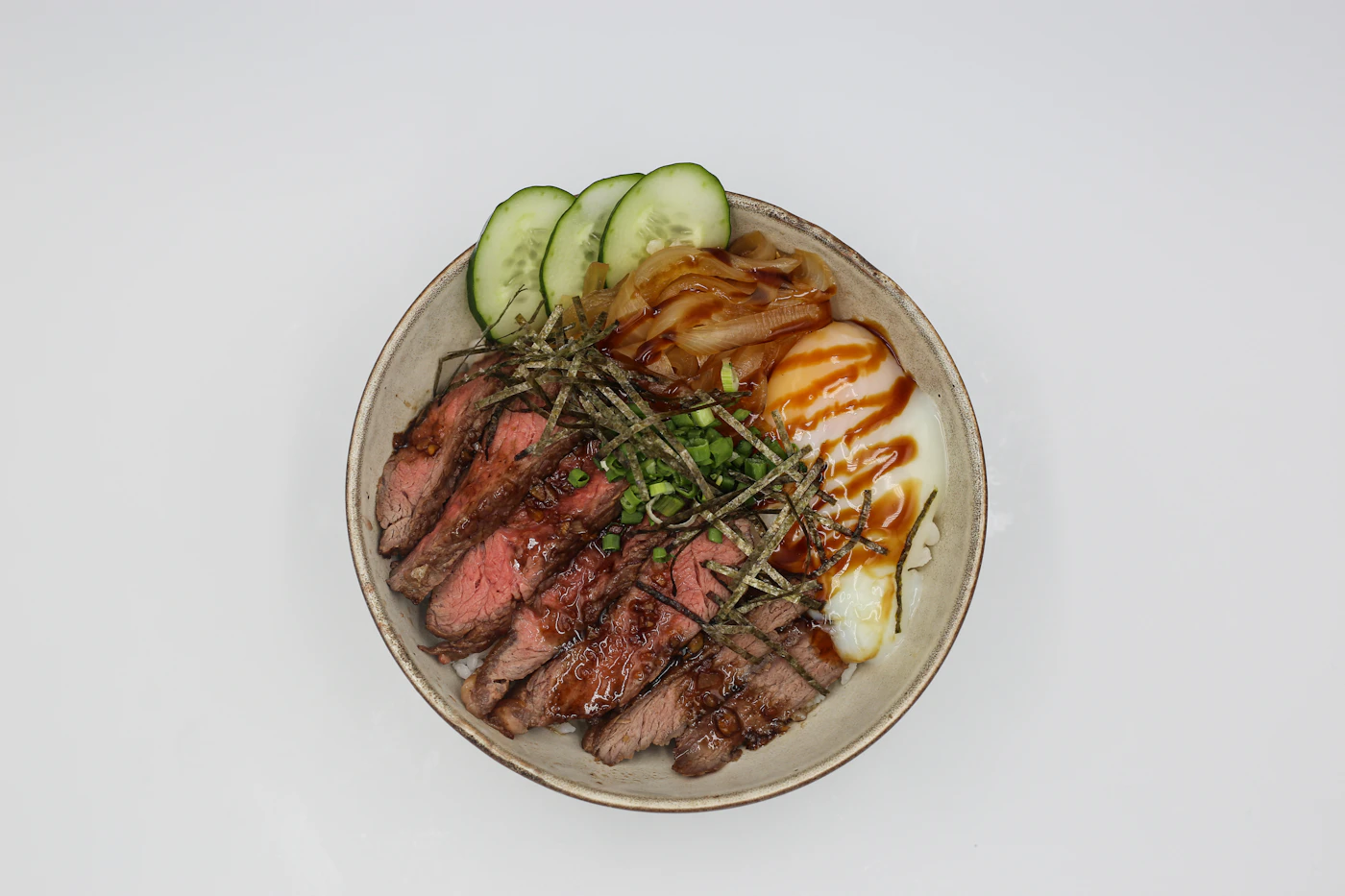 Sliced steak rice bowl with egg cucumber and scallions