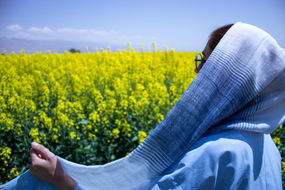 a woman in a blue robe is standing in front of a field of yellow flowers