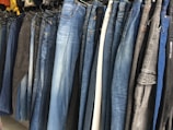 A row of jeans in various shades of blue and black is displayed on hangers in a clothing store. The jeans are arranged closely together, demonstrating a variety of washes and styles, from light blue to dark denim.