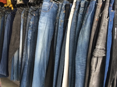 A row of jeans in various shades of blue and black is displayed on hangers in a clothing store. The jeans are arranged closely together, demonstrating a variety of washes and styles, from light blue to dark denim.