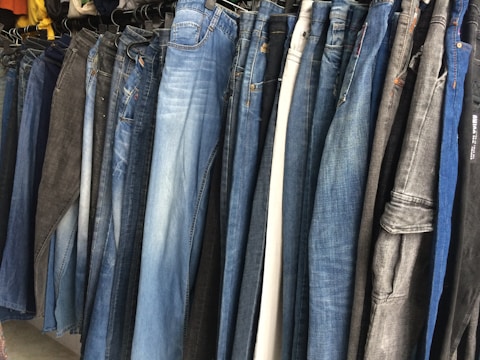 A row of jeans in various shades of blue and black is displayed on hangers in a clothing store. The jeans are arranged closely together, demonstrating a variety of washes and styles, from light blue to dark denim.