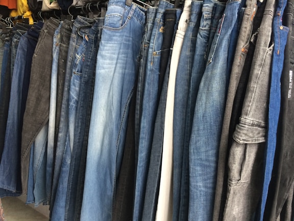 Rows of denim jeans in various washes hanging in a production facility.