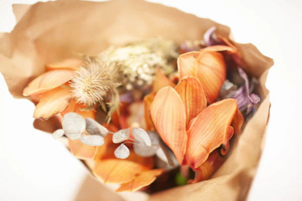 A charming bouquet of mixed seasonal blooms wrapped in brown paper.