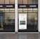 A storefront with large glass windows and multiple signs displaying 'revendo'. Inside, there are visible chairs, plants, and shelves. A poster on the window features the words 'Sell. Repair. Buy.' along with an image of a hand interacting with an electronic device.