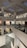 A modern art gallery with multiple levels and open spaces, featuring various artworks on the walls. The structure is illuminated by soft indoor lighting, highlighting paintings and photographs. The gallery features glass railings and a spacious, geometric design.