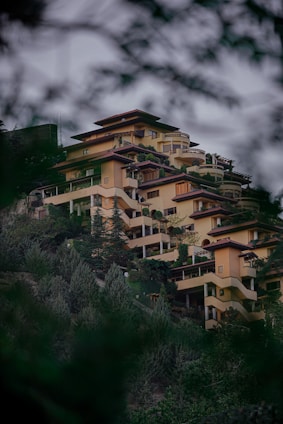 A panoramic view of a modern hillside residence surrounded by lush greenery and traditional Himachali architectural elements.