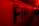 Large capital letters spelling 'FIRE' are prominently featured against a red backdrop. The scene is illuminated with intense red and yellow lighting, creating a dramatic and urgent atmosphere. The setting appears to be indoors, possibly a hallway or tunnel.