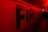 Large capital letters spelling 'FIRE' are prominently featured against a red backdrop. The scene is illuminated with intense red and yellow lighting, creating a dramatic and urgent atmosphere. The setting appears to be indoors, possibly a hallway or tunnel.
