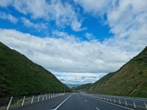 A scenic view of a truck driving on a highway stretching through rolling hills under a clear blue sky.