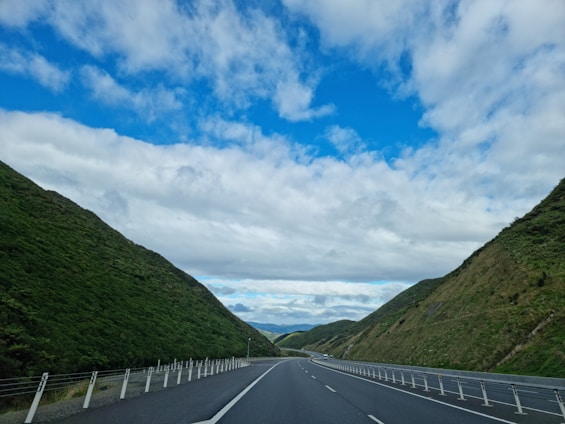 A scenic view of a truck driving on a highway stretching through rolling hills under a clear blue sky.