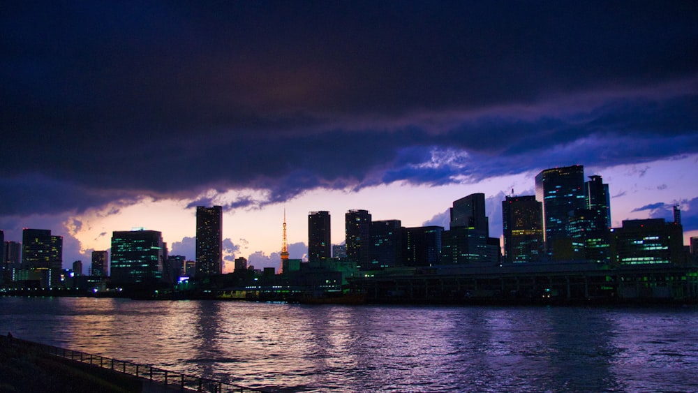 a city skyline at night with a body of water in front of it