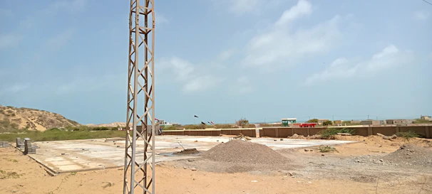 A construction site showing workers reinforcing a large concrete foundation under a clear sky.