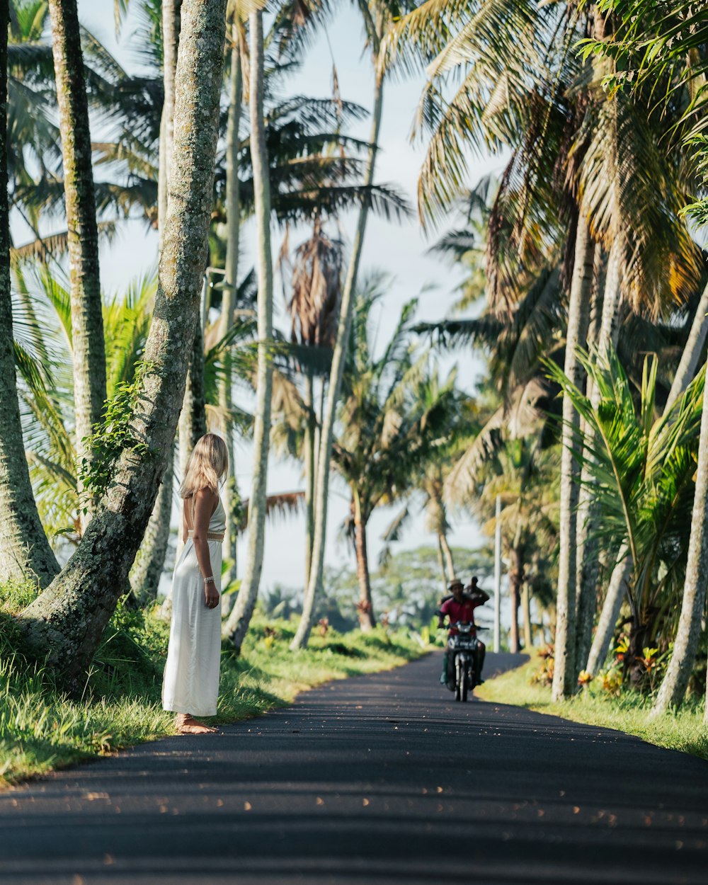 a woman standing on the side of a road next to palm trees