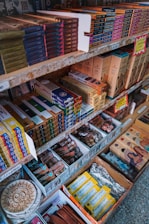 Shelves filled with a variety of incense products, each neatly packed in colorful boxes. The items are organized by brand and type, with price labels visible on the shelves. Decorative elements and promotional signs add to the inviting display.