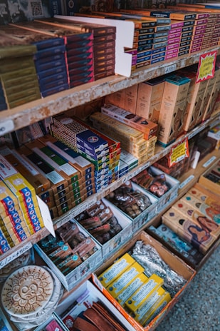 Shelves filled with a variety of incense products, each neatly packed in colorful boxes. The items are organized by brand and type, with price labels visible on the shelves. Decorative elements and promotional signs add to the inviting display.