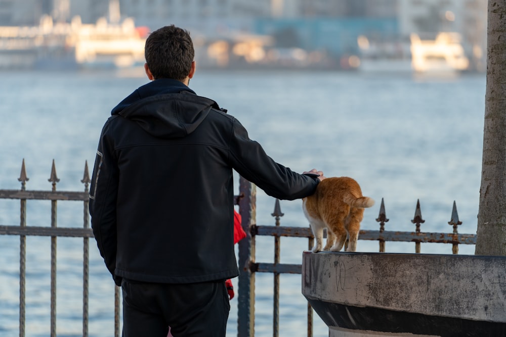 a man standing next to a fence with a cat on top of it