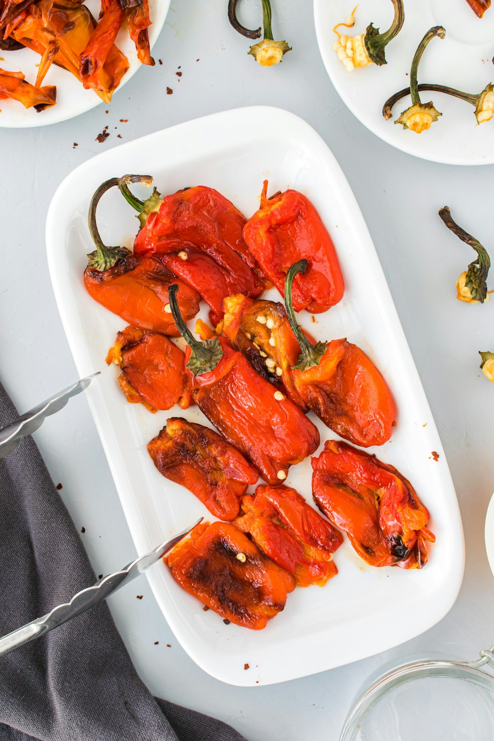 a white plate topped with red peppers next to other plates of food