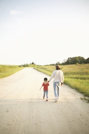 A serene image of a father and daughter walking hand in hand along a quiet path at sunset.