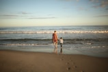 a woman and a child are walking on the beach