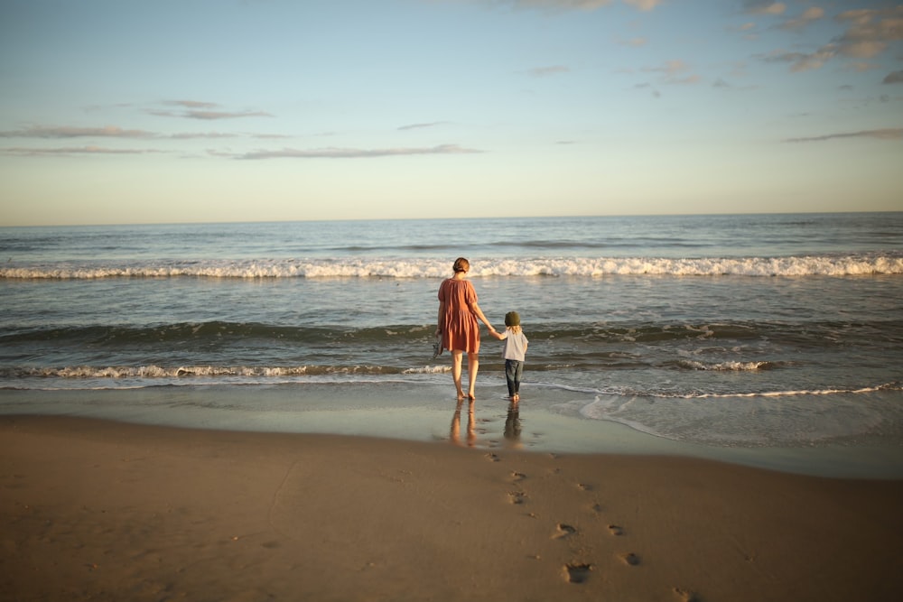 a woman and a child are walking on the beach