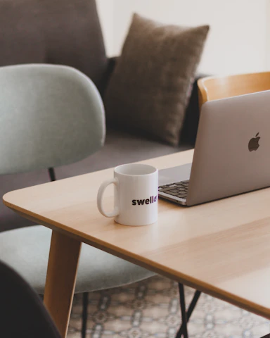 A sleek, minimalist workspace with soft natural light highlighting elegant printed mugs, hoodies, and pillows arranged artfully.