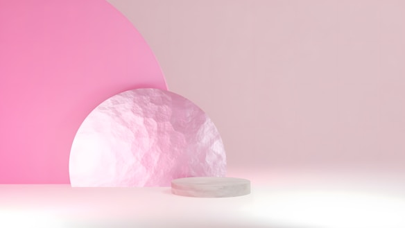 An abstract minimalist composition featuring geometric shapes. The background includes a large pink semicircle and a textured pale pink circle. A small round platform is positioned at the foreground, casting soft shadows.